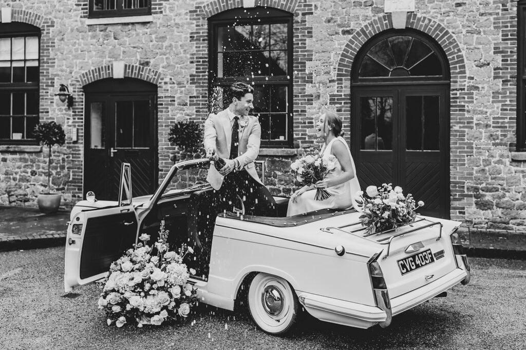 Bride and groom in 1968 Triumph, spraying champagne | Louise Hayes Cake Design | Melissa Megan Photography | Cowdray Wedding