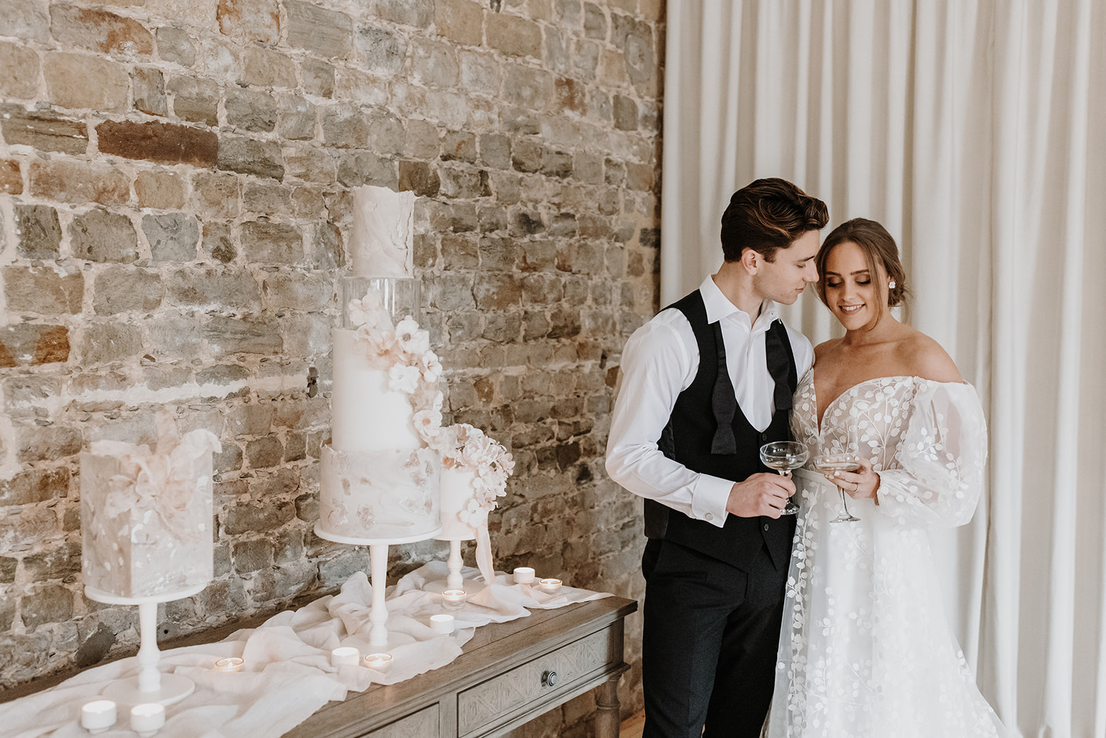 Bride and groom with champagne and a trio of nude, blush contemporary wedding cakes with wafer paper sails and sugar flowers | Louise Hayes Cake Design | Melissa Megan Photography | Cowdray Wedding